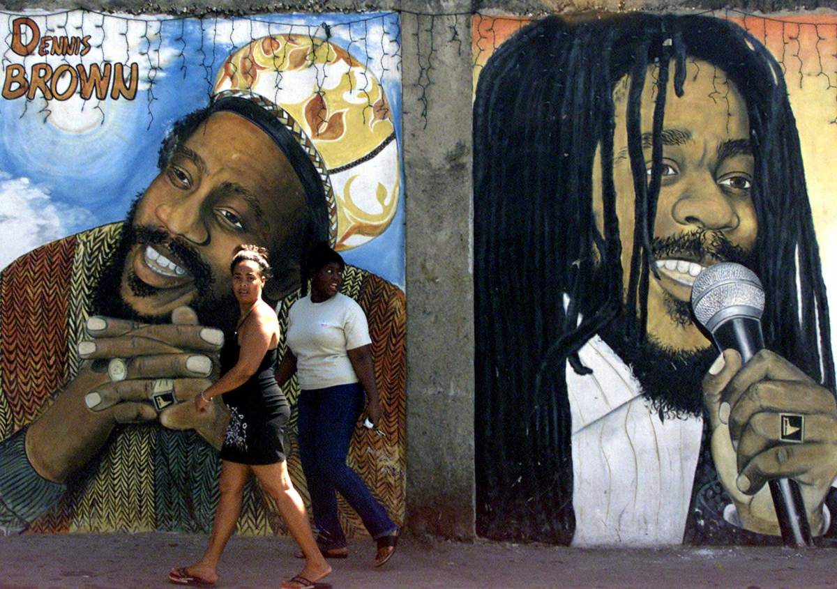 Jamaicans walk in front of a mural of reggae singers Denis Brown (L) and Bob Marley in Kingston Febr..