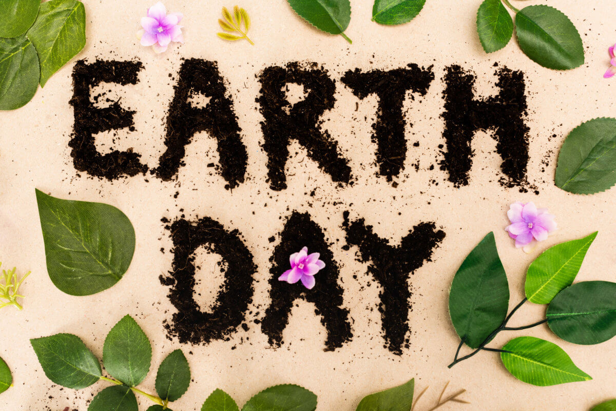 Top view of earth day lettering with leaves and buds on beige background