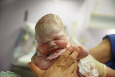 Midwife holding up a vernix covered newborn