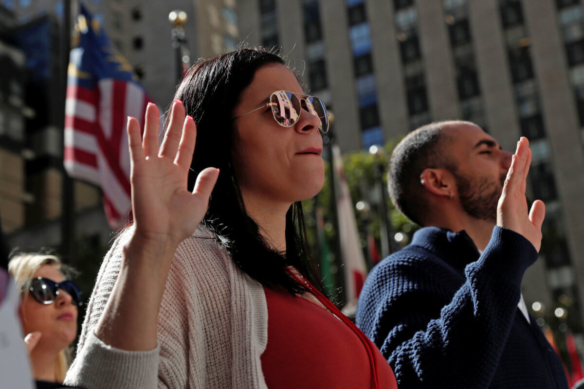 Citizenship candidates raise their hands during the Pledge of Allegiance at the U.S. Citizenship and Immigration Services (USCIS) naturalization ceremony at Rockefeller Plaza in New York City