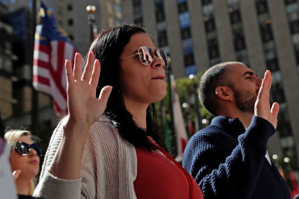 Citizenship candidates raise their hands during the Pledge of Allegiance at the U.S. Citizenship and Immigration Services (USCIS) naturalization ceremony at Rockefeller Plaza in New York City