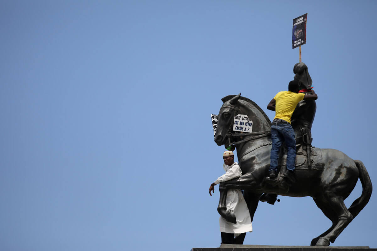 Protesters stand on  the statue of Jean-Jacques Dessalines at the end of a march to demand an investigation into the alleged misuse of Venezuela-sponsored PetroCaribe funds by previous administrations, in Port-au-Prince