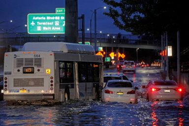 A bus navigates past abandoned cars on a flooded highway in Queens, New York