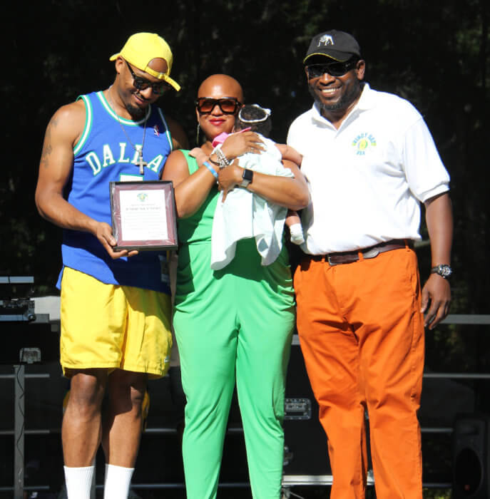 Sharon Jones holds Soca Jones's granddaughter, Khloe, as her brother Eneka "Nekes" Jones, left, receives plaque from Vincy Day USA Committee chairman Raymond Otis Lewis.