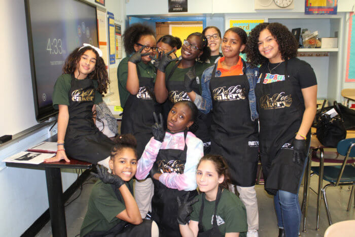 A group of young girls wearing De'Lor Cakery aprons.