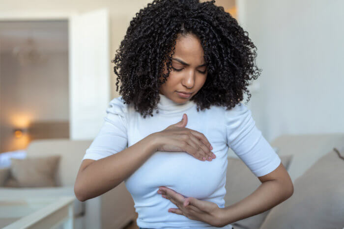 Young African American woman palpating her breast by herself which shows she is concerned about breast cancer.