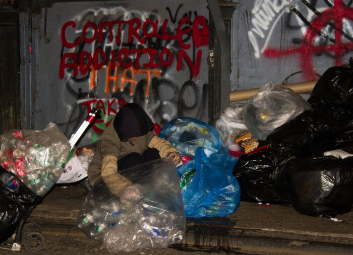 Homeless woman on city street collecting bans and bottles.