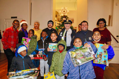 Children are all smiles after choosing their toys at last Saturday's toy giveaway at St. Paul's Lutheran Church, Brooklyn. Pictured are Alumni and NYPD police officers of the 63rd Pc. Community Affairs Department. Backrow, Stanhope Williams, Melnia Cordis, Lorraine Croft Farnell, PO Balkin, Auxiliary Inspector Jeff Zweig, PO Alva, PO Gamba, and Desiree Wharton.