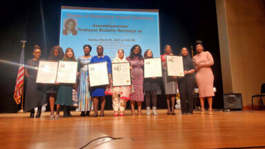 The 2023 Women of Distinction honorees on stage with electeds, holding Proclamations from Assemblymember Rodneyse Bichotte Hermelyn.