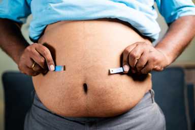 Unrecognizable unhealthy obese man checking stomach or waist fat using measuring tape before diet at home.