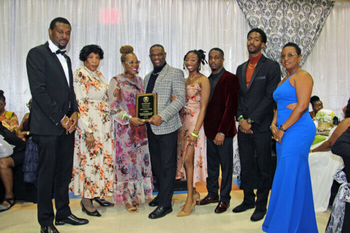 Pastor Derwin Grant, with plaque, flanked by family and church members, and Consul General Rondy "Luta" McIntosh (far left) his wife, Semone (far right).