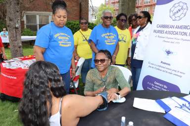 RN Phyllis Payne-Dublin, president of the Caribbean American Nurses Association (CANA) takes a patient's blood pressure while other CANA members look on. 