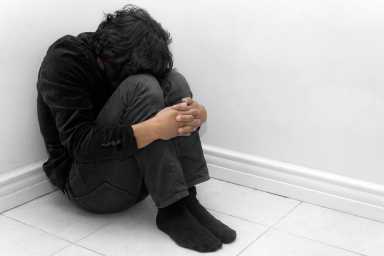 A man in black huddled in a corner