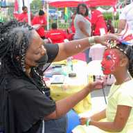 “Kids I Adore” artist, Deloris “Nzingha” Thompson painting the face of a little girl at the Caribbean Heritage Month festivities on Brooklyn Borough Hall Plaza.