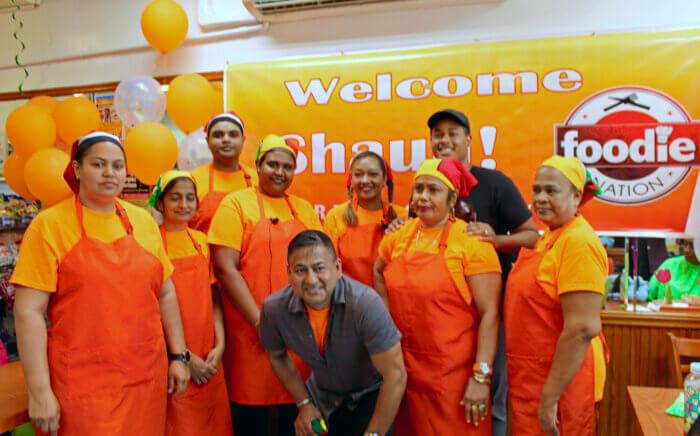 Nohar Singh, owner of ALLFROM1SUPPLIER.COM (front row center stooping), and Trinbagonian foodie nation chef Shaun (back row right), surrounded by kitchen staff after a cooking demonstration and food tasting at Chicken Curry Box, in South Richmond Hill, Queens, to showcase ALLFROM1SUPPLIER.COM a Caribbean cooked food and groceries shipping platform.