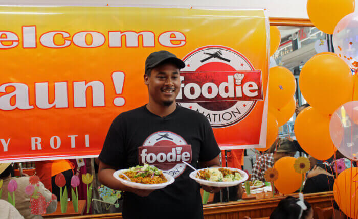 Trinbagonian foodie nation chef Shaun, who has thousands of followers on social media, holding plates of delicious Chicken Pelau, cucumber salad, and potato salad, prepared in Chicken Curry Box the kitchen to promote ALLFROM1SUPPLIER.COM  a Caribbean cooked food and groceries shipping platform.