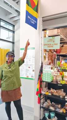 Isra Gordon, owner of Mint Porch Café points to her sign to attract customers to her business, at the intersection of Flatbush (Dr. Roy Hastick Way) and Caton Avenue, Brooklyn.