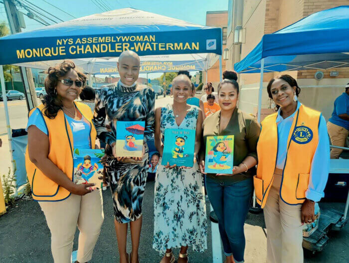 Author of the Peach the Duck book series, Kamla Millwood, second from left, next to Assemblywoman Monique Chandler-Waterman, and Assemblywoman Jamie Williams, with Brooklyn Lions Club Inc. members, showcasing copies of Peach the Duck at the First Annual Folk Festival in the community, on Holy Family Church grounds.