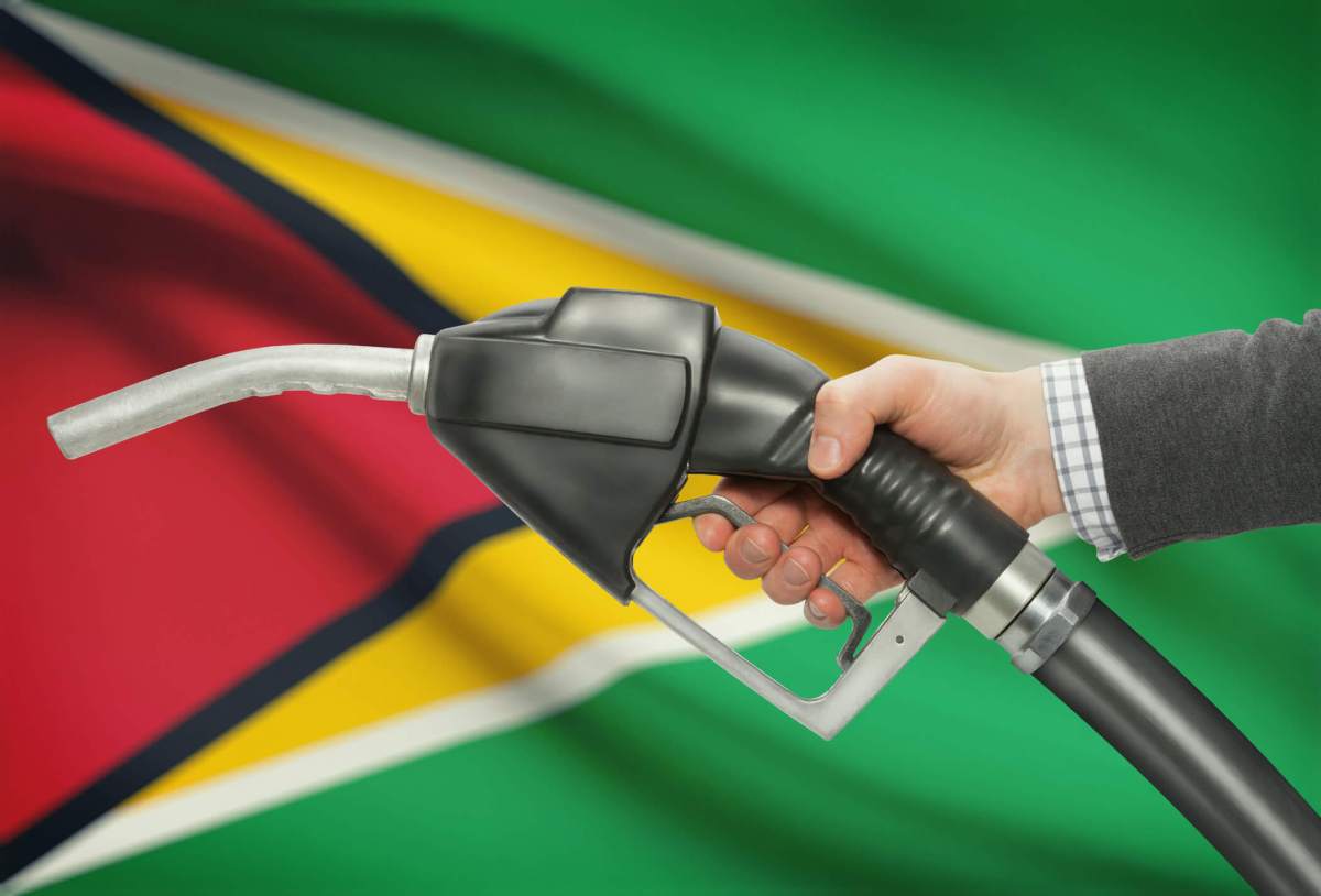 Fuel pump nozzle in hand with national flag on background – Guyana