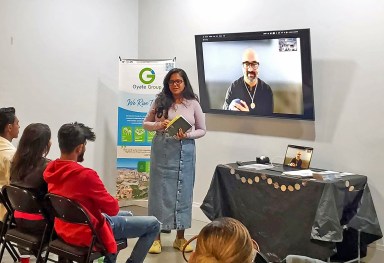 Host Liz Jaikaran at the book launch of “Whales Aria” by Rajiv Mohabir. The author is shown on the video screen.