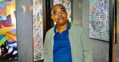 Guyanese-born artist, Carl F. Anderson against the backdrop of his Ribbon Series, during a recent display at the Port Authority, Times Square, NY.