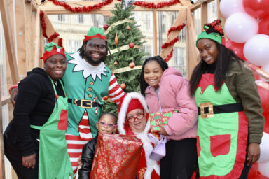 Dale Charles, AKA Mrs. Clause is joined by her elves, and starry-eyed community kids after receiving gifts at the Bed-Stuy Winter Wonderland Christmas at the intersection of Fulton Street and Marcy Avenue.