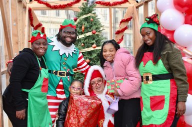 Dale Charles, AKA Mrs. Clause is joined by her elves, and starry-eyed community kids after receiving gifts at the Bed-Stuy Winter Wonderland Christmas at the intersection of Fulton Street and Marcy Avenue.
