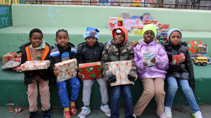 The little ones of Brownsville gleefully show off their Santa gifts on Dec. 23, at a Christmas Bazaar organized by the Divine Explosion Arts Program, at the Love Zone outdoor space.