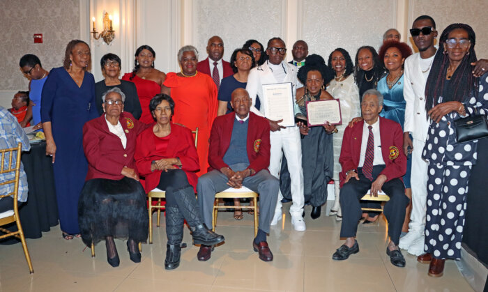 Delroy "Fireman" Hooper, center, in white outfit, holds plaque and proclamation, flanked by his family, elected officials and members of VINCI.