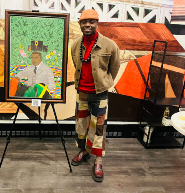 Watson Mere stands in front of a painting of Marcus Garvey entitled "The Complicated Crown,” which represents the complexity of Garvey's legacy.