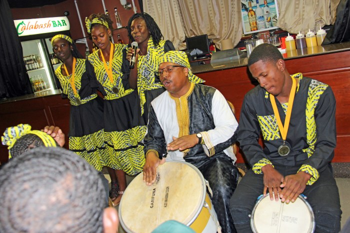 Belizean Alex Colon (l) and Myrick Francis beat drums, and Belize athletes (in background) pay tribute in song, with "You can go, but you must come back," to Aurelio Martinez, a renowned Garifuna artist from Honduras, at a reception in Philadelphia in April 2019 for Belizean athletes at the Penn Relays.