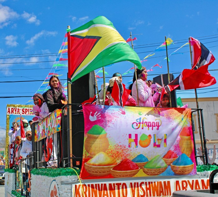 Large Guyana and Trinidad flags are perched atop a sign that says “Happy Holi,” during the 36th Annual Phagwah parade on Liberty Avenue, in Little Guyana on Sunday, April 7, 2024.