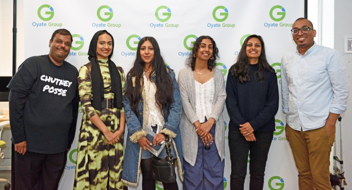 Artists Will Depoo, Raqeebah Zaman, Jasmine Baksh, Nadia Misir, Nazrina Rodjan and Oyate Group's COO Jason Autar pose in front of the step and repeat.