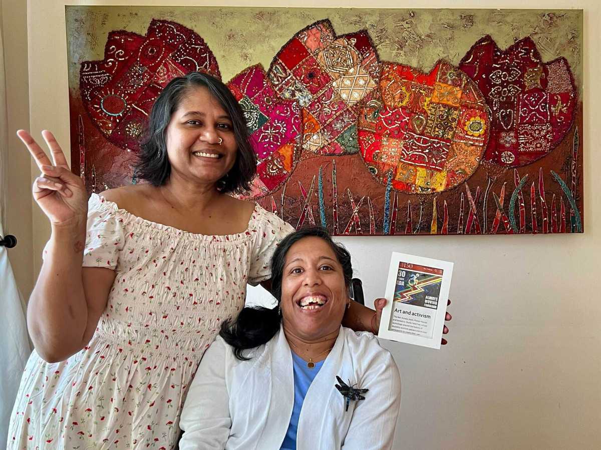 Lakshmee Lacchman-Persad (left) and her sister Annie Lachhman in front of a colorful painting.
