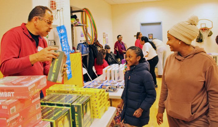Jonathan Locke, a craftsman and owner of Timehri Arts, a former student of Bishops High School, hands over a toy to a starry-eyed little girl as her mom looks on with a smile at a Toy giveaway hosted by Guyana St. Roses Alumni Association USA, in partnership with President's College Alumni Association Inc, and Guyanese in the Diaspora Inc, at PS/IS 109 in Brooklyn, last Saturday.