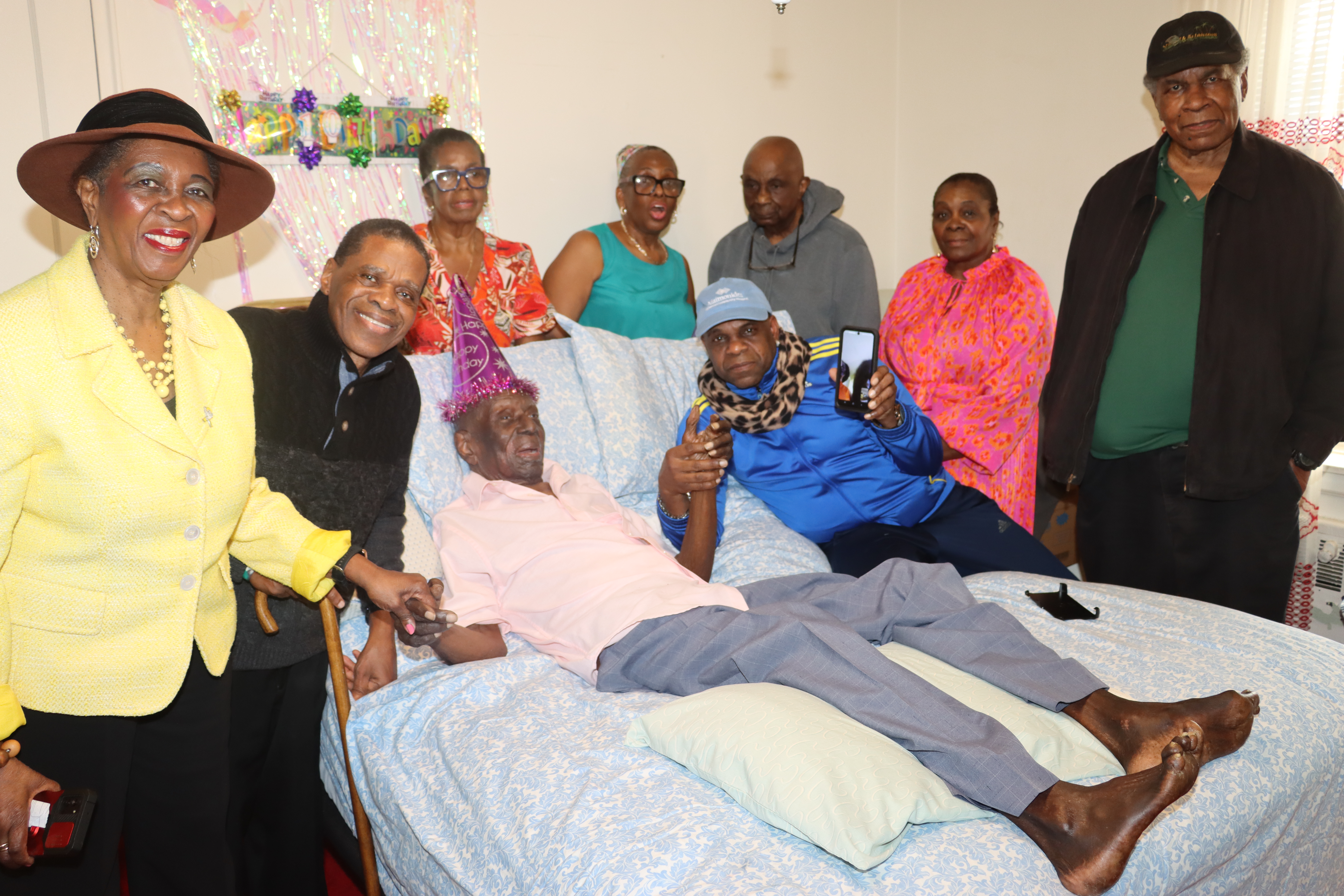 Family members, friends and well-wishers flank Mitchinson "Mitchie" James as he lays in bed