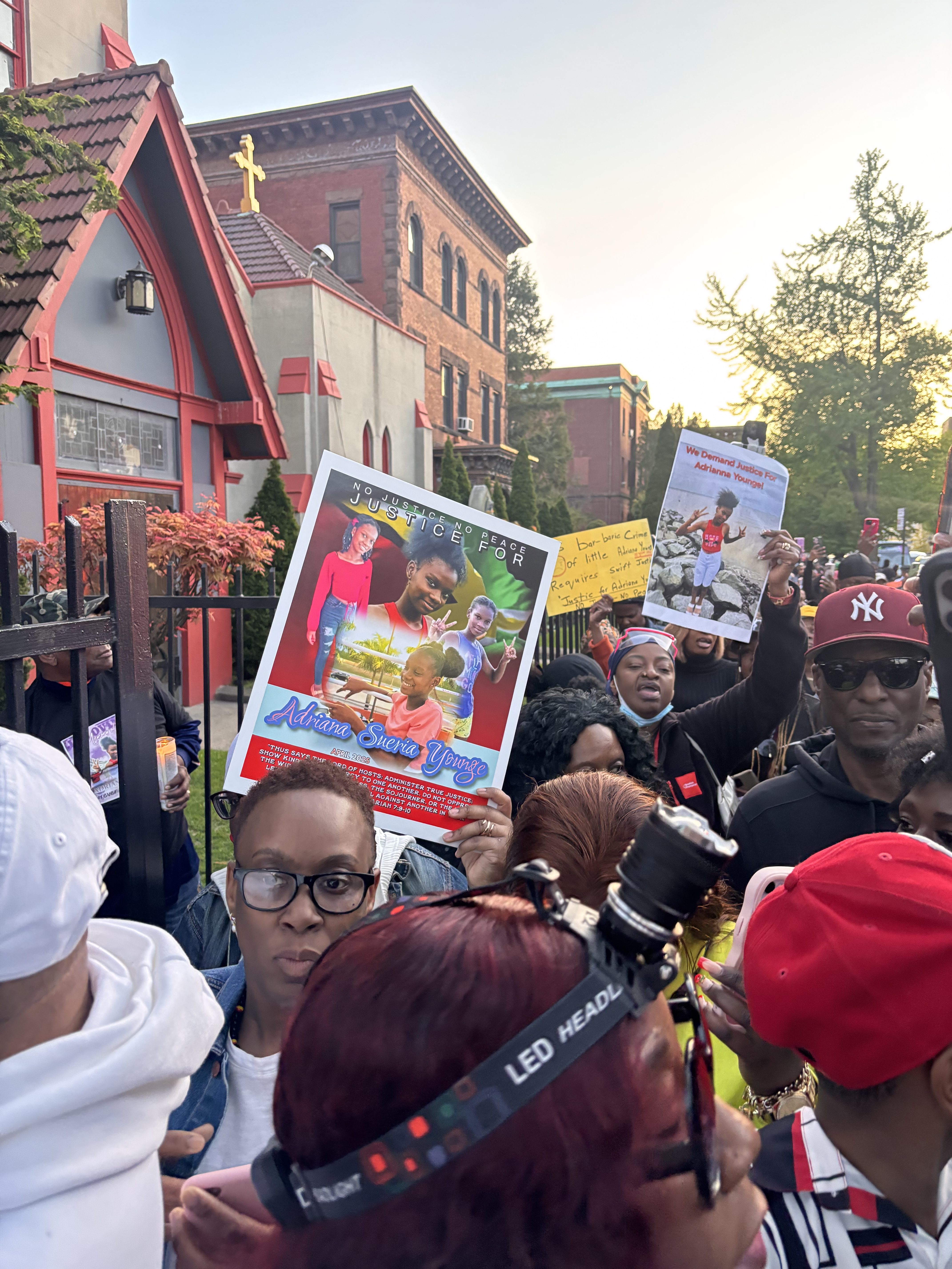 Attendees hold signs with images of Adrianna Younge during a vigil in Brooklyn, part of a growing international movement demanding justice in her case.
