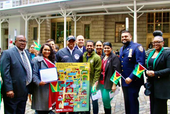 Consul General Ambassador Michael E. Brotherson, Bharati Kemraj (with Mayor's office Citation) Mayor Eric L. Adams, Manuel Castro, Richard David, First Deputy Commissioner Tania Kinsella, Sookranie Dhanpat, NYPD Officer, and Marcia Martinez, pictured with the Guyana Gateway in Brooklyn & Little Guyana in Queens and the Bronx immigrant poster, in honor of the country's 59th Independence Anniversary, flag raising on May 23.