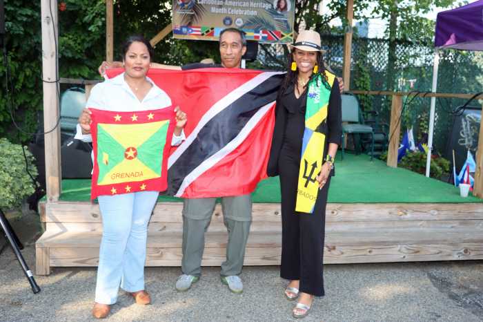 Golden Touch DJ Chinee displays Trinidadian flag flanked by Assembly Member Jaime Williams, left, showing Grenadian flag, and Assembly Member Monique Chandler-Waterman, with scarf in Barbadian and Jamaican national colors.