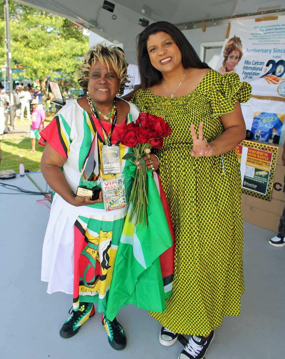 President of the Guyana American Heritage Foundation, Lady Ira Lewis, all smiles, with a glass statue and bouquet of flowers received from Senator Britnee Timberlake, showing a peace sign at the July 13 Annual Guyana Caribbean Family Fund Day at Monte Irvin Orange Park, Orange, New Jersey.