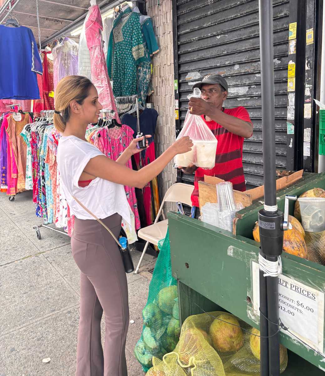 A vendor hands two bowls of fresh coconut water to a customer on Liberty Avenue, Queens, where demand for this thirst quencher peaks in the summer.