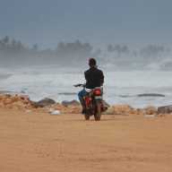 Man on motorcycle rides on beach past heavy waves from Hurricane Erin