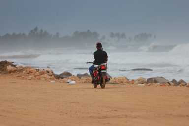 Man on motorcycle rides on beach past heavy waves from Hurricane Erin