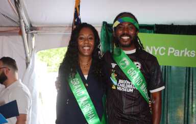 Roxaane Joseph and Atiba Edwards smile for a photo while wearing green ribbons to represent their roles as grand marshals at the Caribbean Carnival Parade.