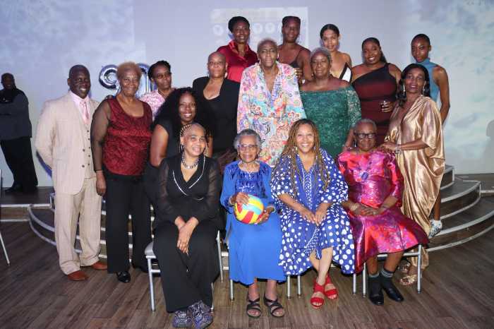 Gloria Lewis holds netball, flanked by former netballers and a coach, far left.