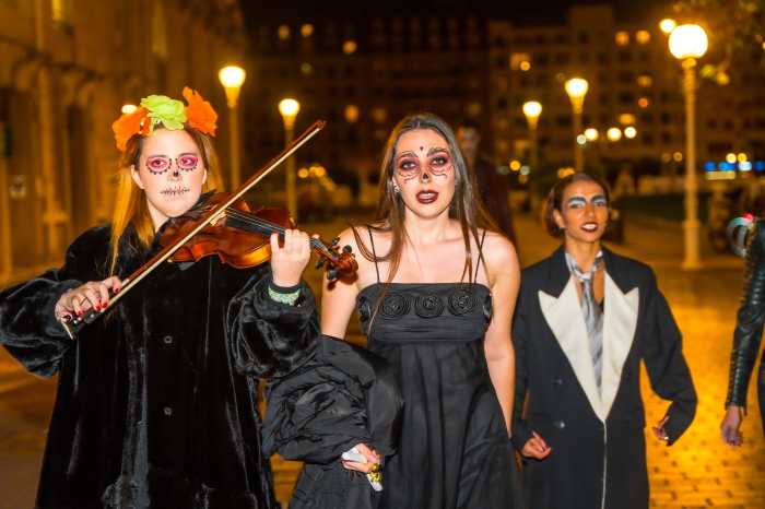 A group of people dressed in Halloween costumes walking down a street with one of them playing a violin.