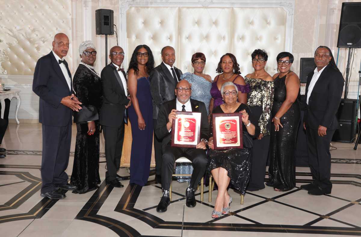 Sitting in front with plaques, journalist and humanitarian Michael Wattkis and Dr. Montrae Calhoun Thomas, a pediatrician in New Jersey who were honored at the Caribbean Medical Mission (CMM) Black Tie gala in NJ. Looking on are some of the board members of the CMM.