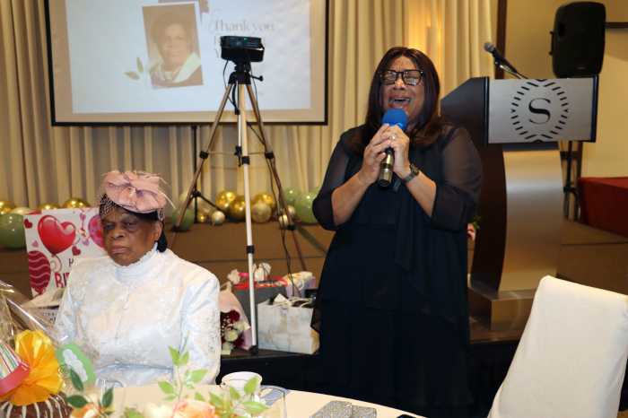 Pastor Neithe E. Soleyn, seated, listens, as her eldest daughter, Susanne Young, sings "Don't Leave Behind an Unfinished Task.”