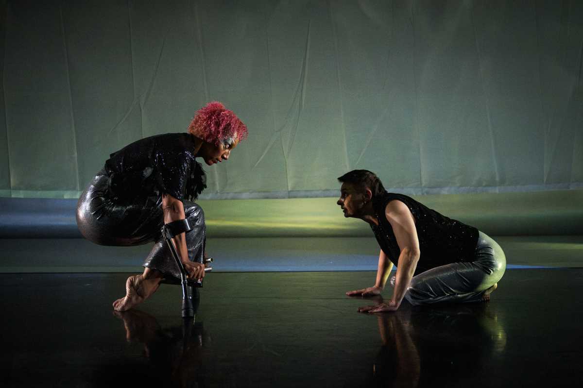 Alice and Tati face off. Alice is balancing on her short crutches, legs bent and folded under herself, tops of her toes grazing the floor. They peer at each other with curiosity and intensity.