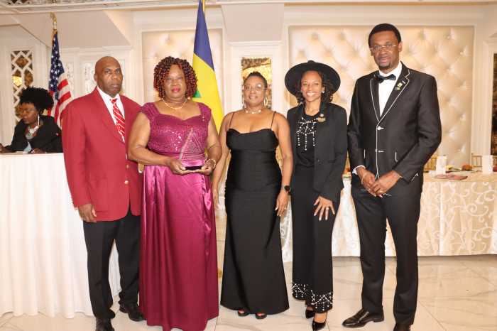 Pamella Ferrari-Easter receives an award, flanked by Wayne Raggeutte, left, Assembly Member Monique Chandler-Waterman, fourth from left, Consul General Rondy "Luta" McIntosh, right, and his wife, Semone, third from left.